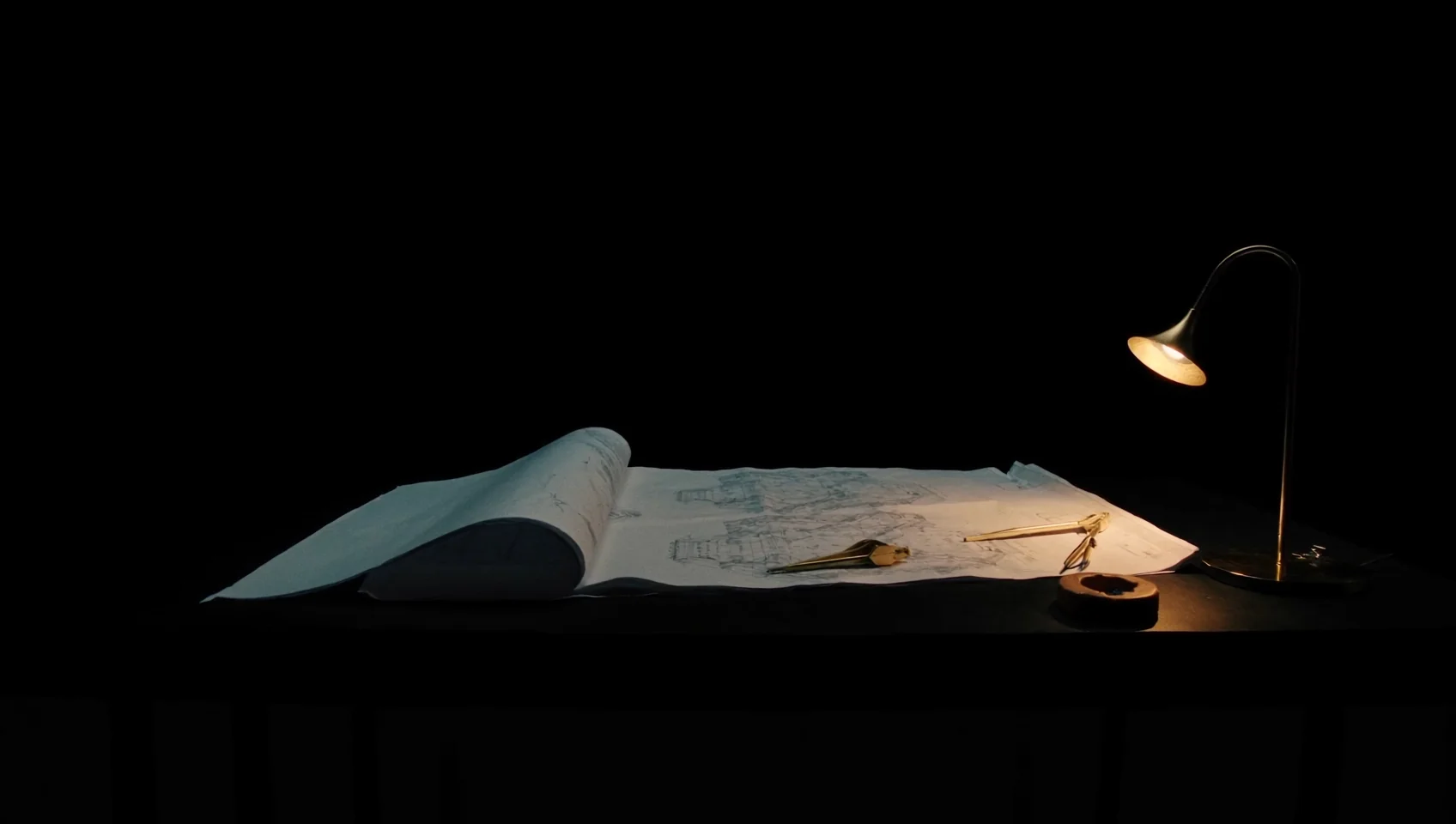 Planos desplegados sobre una mesa, iluminados por una lámpara